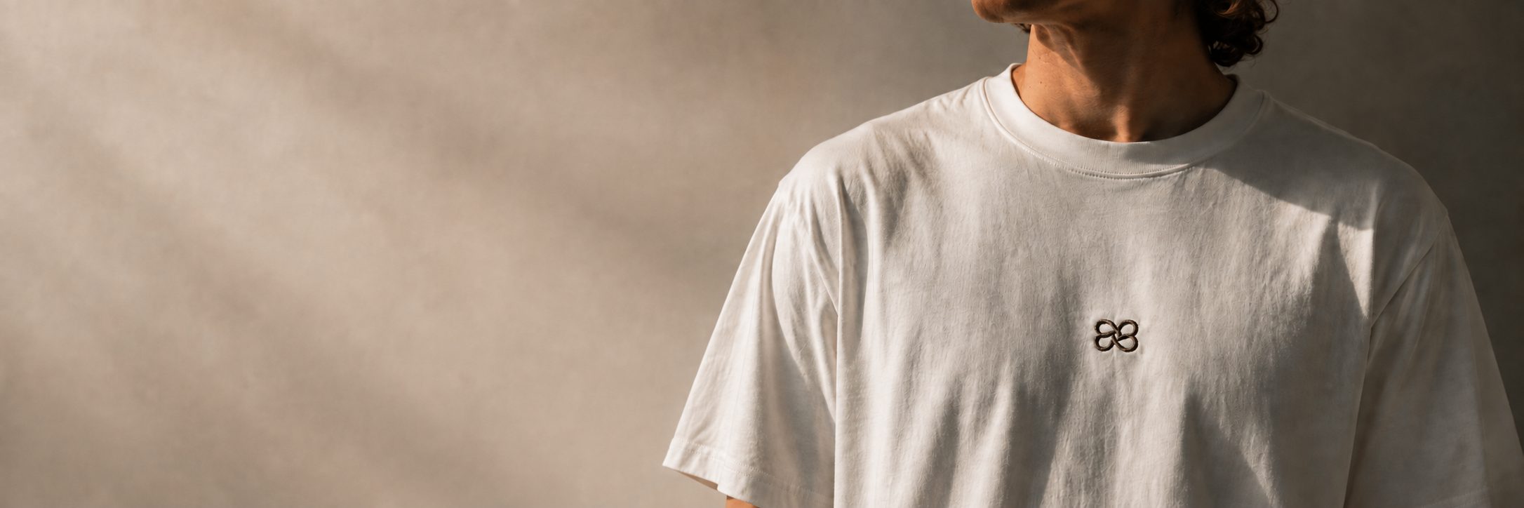 Emblème Consonance brodé au fil grenat sur le devant d’un t-shirt blanc cassé